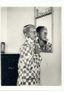 Black and white photo of a woman standing by the wall. Her figure is reflected in the mirror