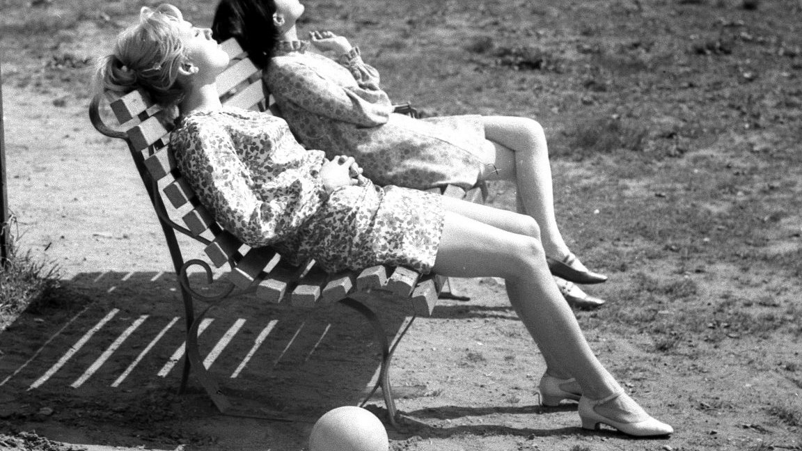 Black and white picture of two women sitting relaxed on a bench and sunbathing