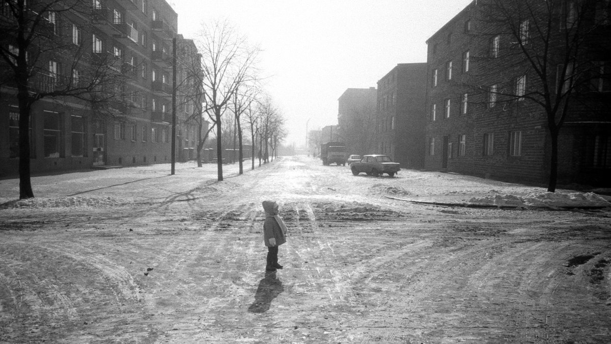 Black and white winter picture of a crossroad. An about three-year-old child wearing warm clothes is standing in the middle of a crossroad.