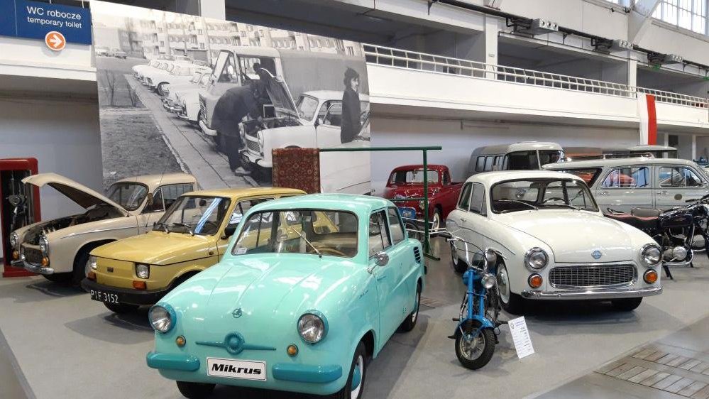A photo from the exhibition: four cars from PRL period. In the background a black and white photo from that times (cars parked by the pavement, a man repairing one of them).