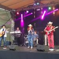 Picture of a country group - singing woman and two men playing the guitars on a stage. In the background a man playing drums and a man playing keyboard.