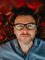 Photo of the artist - man in glasses in blue shirt on red background