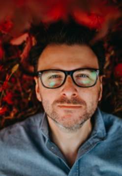 Photo of the artist - man in glasses in blue shirt on red background