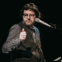 Photo of the artist - a man standing by the microphone. Black background.