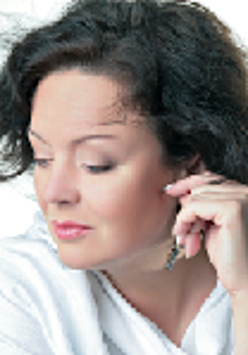 Photo of the face of the singer dressed in white blouse and looking down with her hand touching her ear