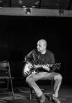 Black and white photo of a man sitting on chair and playing the guitar
