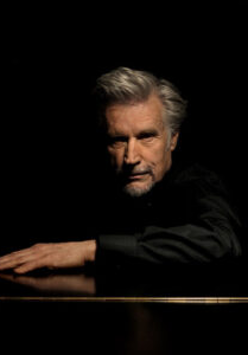 Photo of the artist - a man in black clothes on the black background