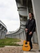A man leaning against bridge pillar, holding a guitar