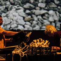 The photo shows the musicians during a performance, leaning over electronic instruments