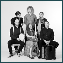 The black and white photograph shows the six members of the Okra team in two rows. In the first one, a woman and two men are sitting on chairs. Behind them are two more ladies and one gentleman. Some of them hold musical instruments.