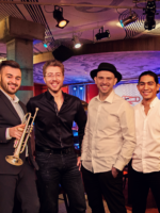 Photo of a band - four man, one of them is holding trumpet