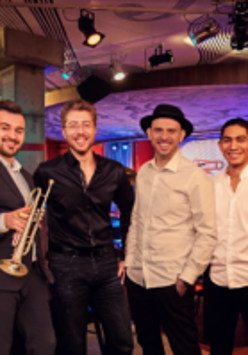 Photo of a band - four man, one of them is holding trumpet
