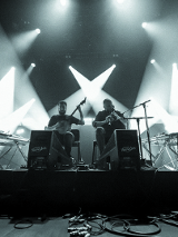 The black and white photo taken during the concert, from under the stage. In its central part there are two musicians - one plays the banjo and the other plays the bagpipes.