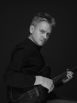 Black and white photo of the musician - a man holding a guitar and looking into the camera