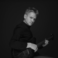 Black and white photo of the musician - a man holding a guitar and looking into the camera