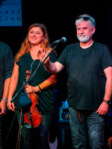 Three men and a woman standing on stage. A woman is holding the violin.