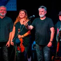 Three men and a woman standing on stage. A woman is holding the violin.