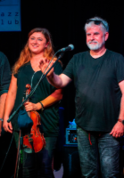 Three men and a woman standing on stage. A woman is holding the violin.