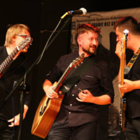 Three men playing guitars on a stage