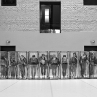 Black and white photo of the dancers in a row, who are standing in transparent boxes.