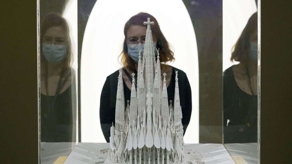A mockup of Gaudi's cathedral in a glass case and a woman watching it.