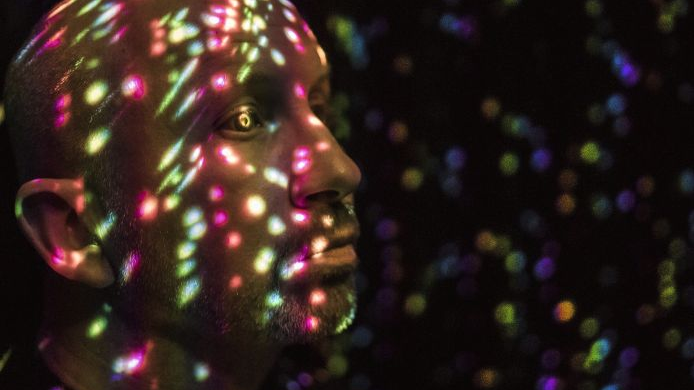 Photo of a man's face on which colourful light points are visible.