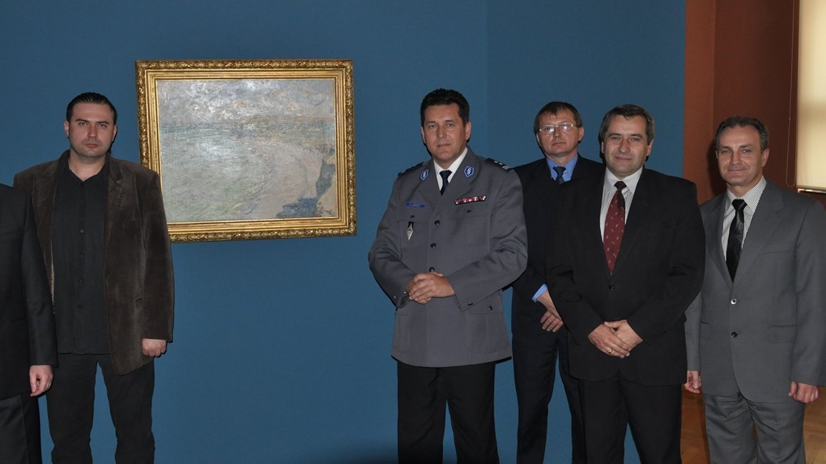 Five men looking at the camera, in the background the picture "Beach in Pourville" in golden frame on blue wall