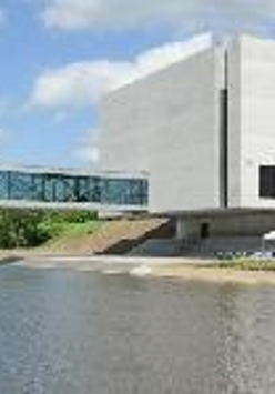 Photo of Porta Posnania: a concrete building by a river.