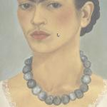 A woman with dark hair tied in a bun. The woman has a light blouse with lace trim and a necklace of dark beads. The background is dark gray.