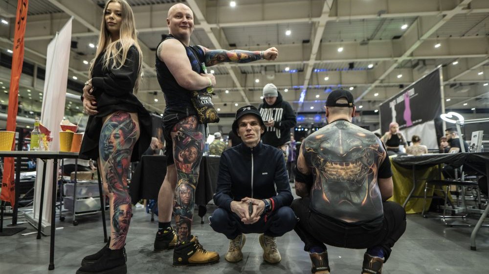 Four tattooed people pose for a photo in a large, spacious hall.