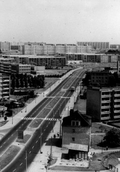 A black and white photograph of a bird's eye view of a landscape with apartment blocks and a two-lane road running diagonally