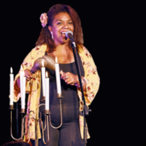Picture of the singer - afro american woman standing and singing to a microphone; a woman holds maracas in her hands