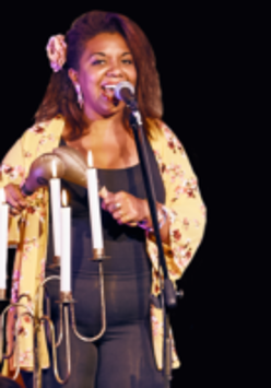 Picture of the singer - afro american woman standing and singing to a microphone; a woman holds maracas in her hands