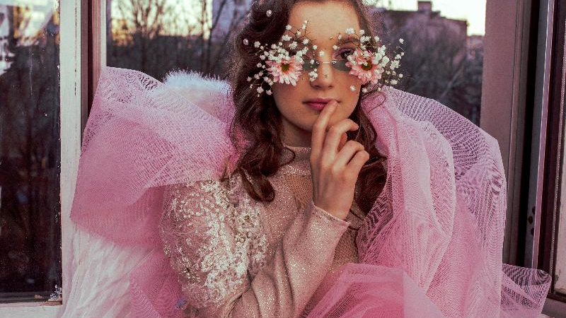 Picture of young woman dressed in pink garment in glasses decorated with flowers.