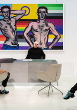 Photo of two men, one sitting at the desk, another opposite him in an arm-chair. Colourful picture on the wall as a background.