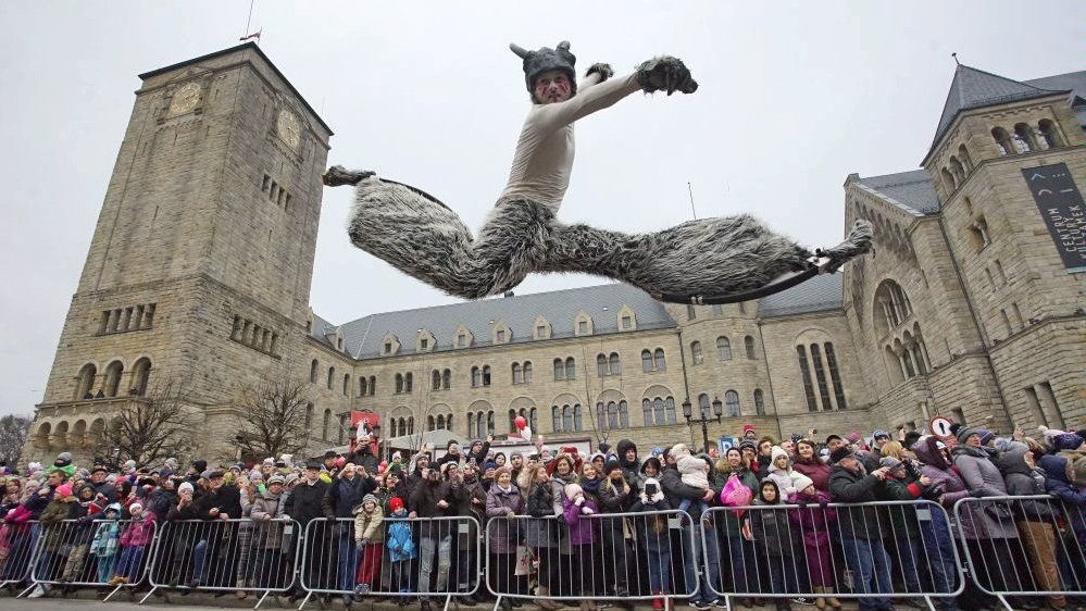 Photo from one of the previous St. Martin parade: a man performing on a street jumping high and people watching the show. The building of the Castle Culture Centre in a background.