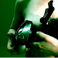 Photo of a naked woman who is holding a black metal object. Green background.