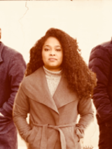 Photo of the band - a woman in the middle and two men on left and right behind the woman