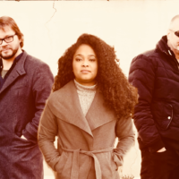 Photo of the band - a woman in the middle and two men on left and right behind the woman