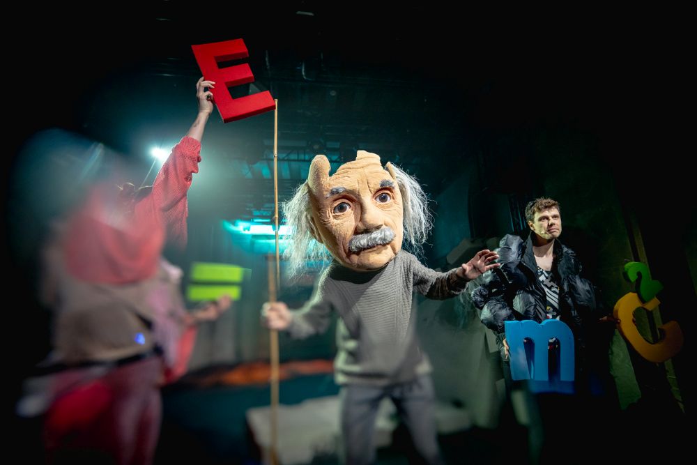 Aktor z przeskalowaną głową-maską Alberta Einsteina stoi na środku sceny.