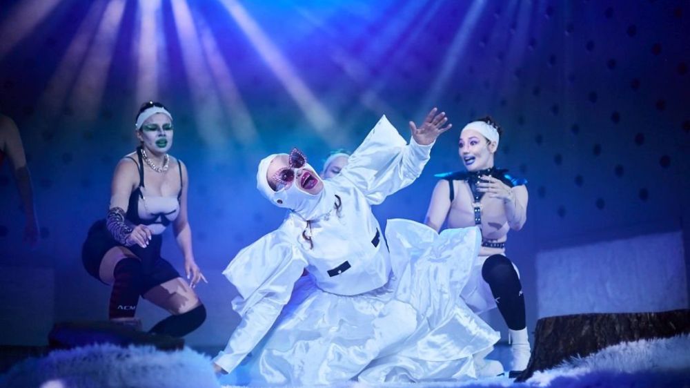 Aktorki w białych kostiumach i wyrazistym makijażu na scenie.