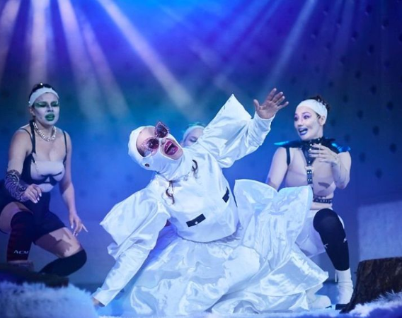 Aktorki w białych kostiumach i wyrazistym makijażu na scenie.