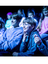 Na zdjęciu nastolatki siedzące w kinie, patrzą na ekran, śmieją się.