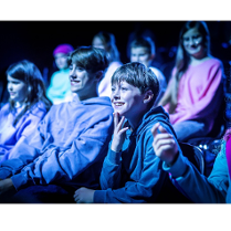 Na zdjęciu nastolatki siedzące w kinie, patrzą na ekran, śmieją się.