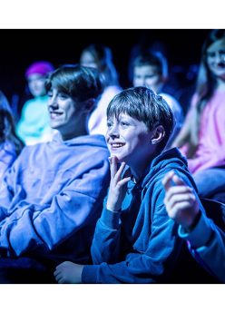 Na zdjęciu nastolatki siedzące w kinie, patrzą na ekran, śmieją się.
