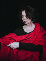 Kobieta w czarno-czerwonym stroju stoi na ciemnym tle.