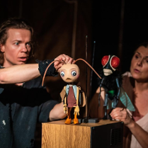 Zdjęcie z występu, na którym widoczni są aktorzy sterujący drewnianymi figurkami owadów.
