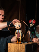 Zdjęcie z występu, na którym widoczni są aktorzy sterujący drewnianymi figurkami owadów.