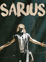 Na zdjęciu widać artystę z rozłożonymi rękoma i zadartą do góry głową.