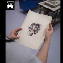 Na zdjęciu widać dłonie uczestnika pracowni, trzymające czarno-białą grafikę.